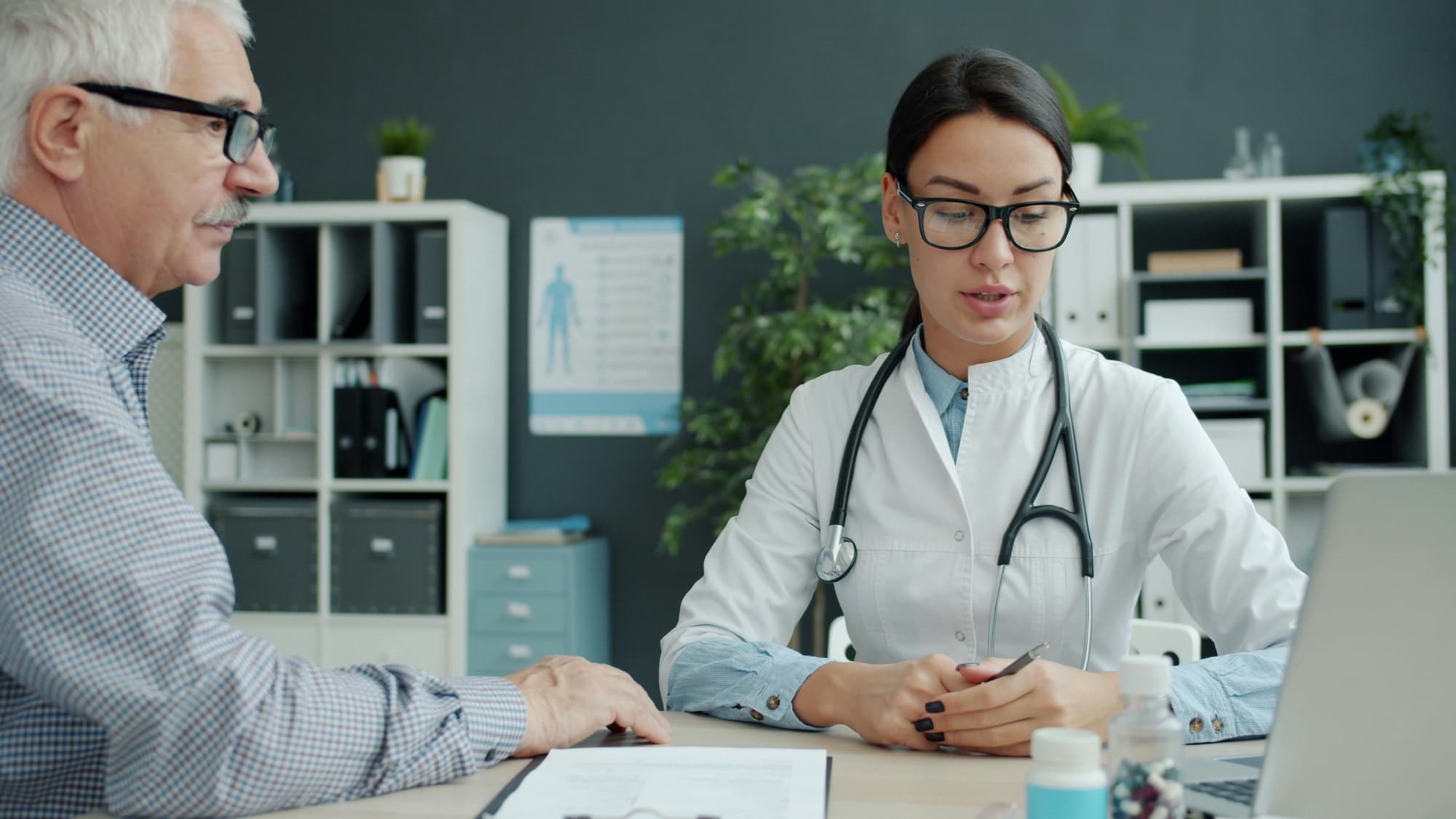 Physician in a white coat consulting with an older patient at her desk